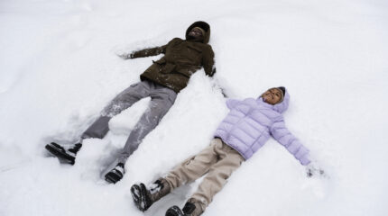 Pai e filha brincando na neve - Viajar com Crianças no Inverno - young-girl-making-snow-angels-with-her-father-winter Viagem para a neve com filhos crescidos: um convite à conexão na transição para a adolescência